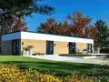 Nowoczesny dom modułowy 100m2 cena pod klucz, z drewnianą elewacją i dużymi przeszkleniami, otoczony zielenią i jesiennymi drzewami.