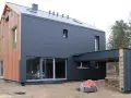Nowoczesny dom w trakcie budowy, z ciemnoszarą elewacją z **struktonitu** i widocznymi elementami konstrukcyjnymi.
