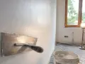 Nakładanie gładzi na ścianę za pomocą kielni. W tle okno i lampa budowlana.