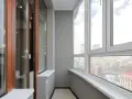 Wnętrze loggii z widokiem na miasto. Drewniane drzwi balkonowe i duże okna wychodzą na zabudowania.