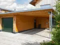 Drewniana wiata przy domu z zieloną bramą garażową i miejscem na samochód.