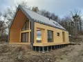 Nowoczesny dom 70m2 z drewnianą elewacją i dużymi oknami, otoczony lasem.