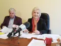 Dwoje ludzi przy biurku z mikrofonami i dokumentami.