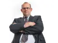 Mężczyzna w garniturze i okularach ze skrzyżowanymi rękami.