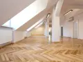 Jasne, przestronne poddasze z drewnianą podłogą w jodełkę. Widoczna ścianka kolankowa, okna dachowe i grzejnik.