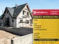 Tablica informacyjna budowy domu w trakcie prac. Widoczny dom w rusztowaniach i betonowy murek.