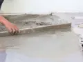 Ręka wyrównuje świeży beton, tworząc idealnie gładką podłogę na gruncie.