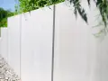 Nowoczesny, tani murek oporowy z betonu, otoczony zielenią i żwirem, tworzy estetyczne i funkcjonalne ogrodzenie.