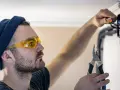 Elektryk w okularach ochronnych i czapce z wąsem, trzymający kombinerki, sprawdza, z której strony faza w gniazdku.