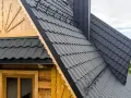 Nowoczesny dach mansardowy z ciemnoszarej blachodachówki, otoczony zielenią i malowniczym krajobrazem.