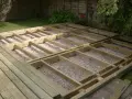 Drewniana konstrukcja pod taras z widocznymi legarami i podsypką żwirową. Wymiary legarów są kluczowe dla stabilności.