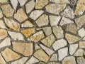 Chropowata ściana z nieregularnych, żółtawych i białych kamieni piaskowca, połączonych ciemnym cementem.