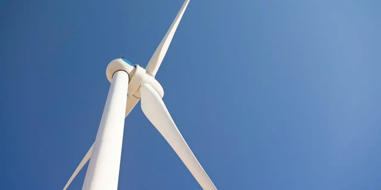 Białe turbiny wiatrowe obracają się na tle błękitnego nieba, czerpiąc energię z wiatru.