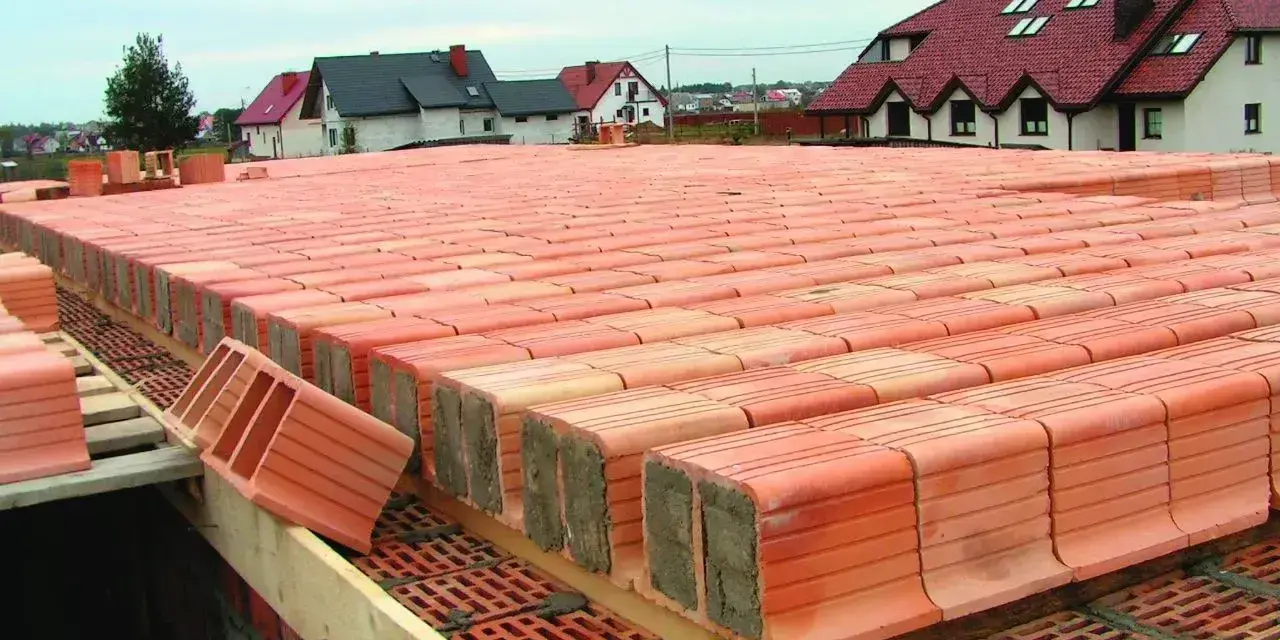 Budowa stropu ackermana z pustaków ceramicznych. W tle domy jednorodzinne.