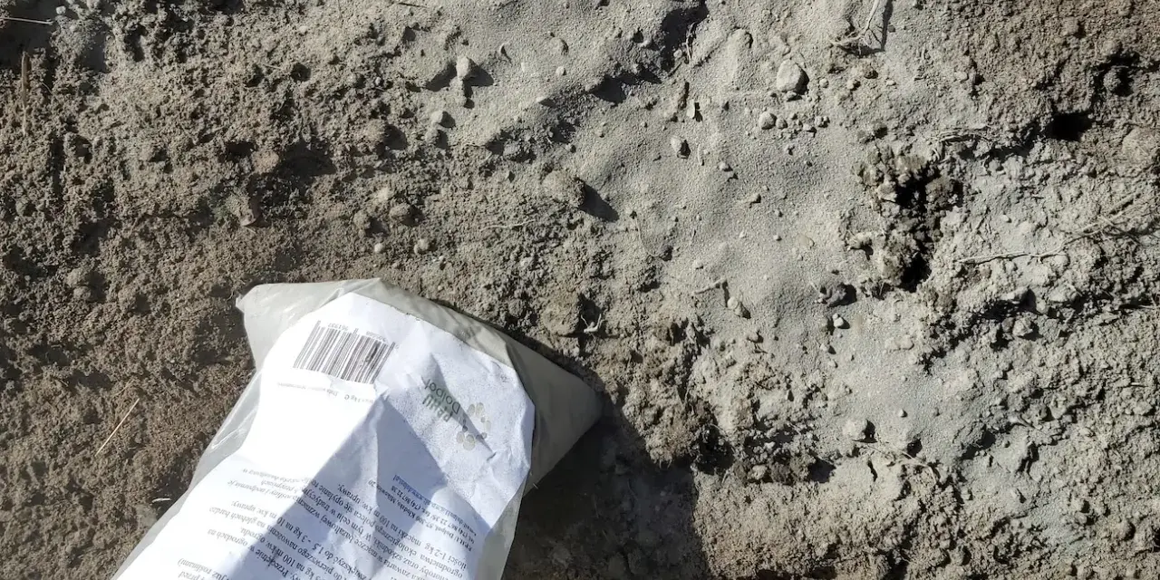 Opakowanie mączki bazaltowej leży na ziemi, gotowe do zastosowania w ogrodzie.