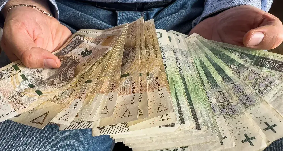 Ręce trzymające plik banknotów 100 zł i 200 zł. To może być darowizna 100 tysięcy od rodziców na nowy dom.