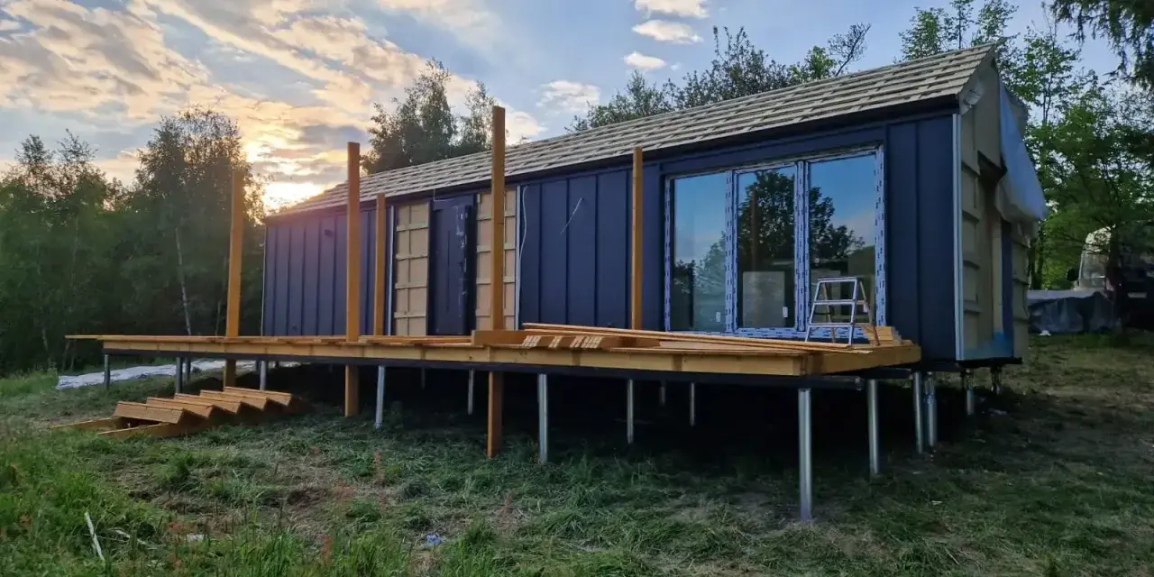 Nowy bungalow na palach, z drewnianym tarasem i dużymi oknami, w trakcie budowy.