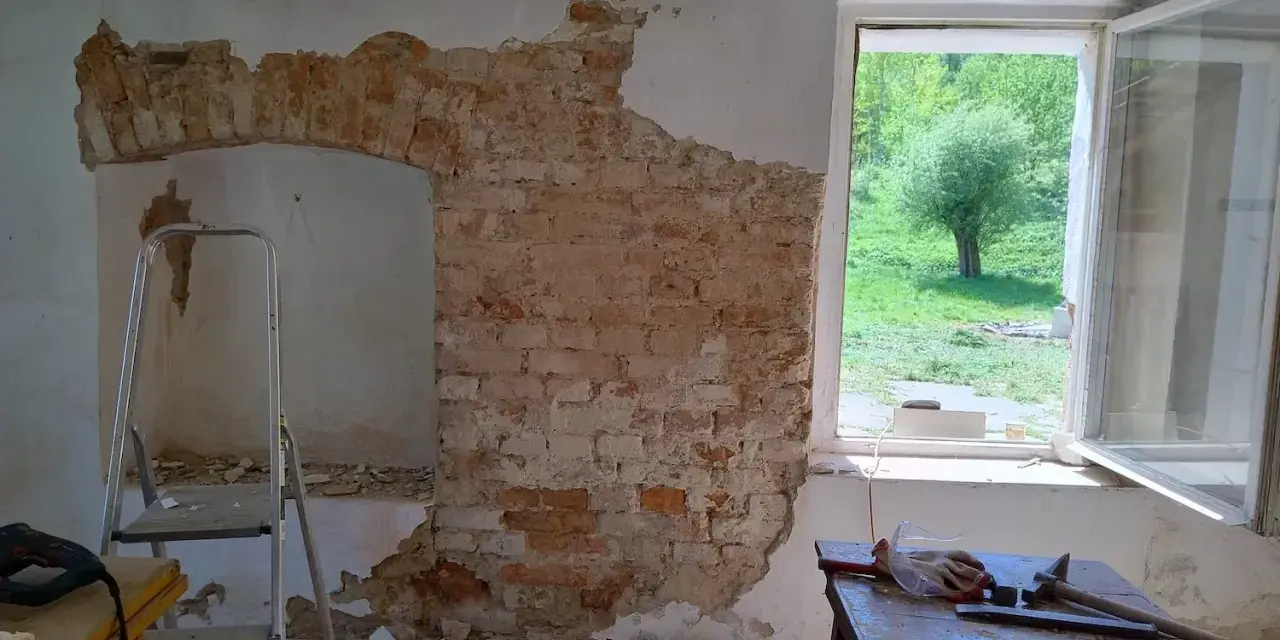 Odkryty mur pruski w trakcie remontu. Widać cegły, gruz, drabinę i narzędzia.