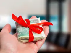 Dłoń trzyma plik banknotów przewiązany czerwoną wstążką. To prezent, kiedy nie trzeba zgłaszać darowizny do urzędu skarbowego.