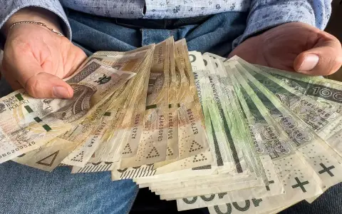 Ręce trzymające plik banknotów 100 zł i 200 zł. To może być darowizna 100 tysięcy od rodziców na nowy dom.