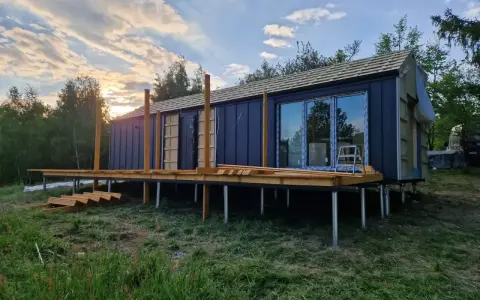 Nowy bungalow na palach, z drewnianym tarasem i dużymi oknami, w trakcie budowy.