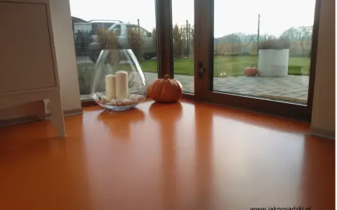 Pomarańczowa podłoga z żywicy, z widocznym blaskiem i odbiciami. Wazon ze świecami i dynia dodają jesiennego klimatu.