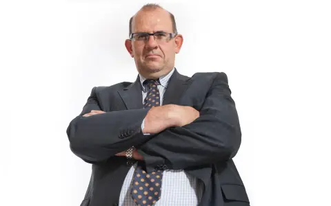 Mężczyzna w garniturze i okularach ze skrzyżowanymi rękami.