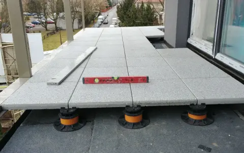 Układanie tarasu wentylowanego. Sprawdzanie poziomu płyt. Cena za m2 zależy od materiału i systemu montażu.