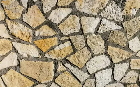 Chropowata ściana z nieregularnych, żółtawych i białych kamieni piaskowca, połączonych ciemnym cementem.