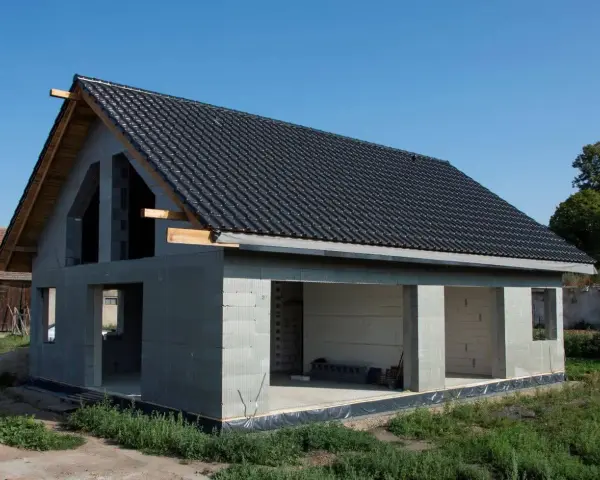 Dom w stanie surowym otwartym, z dachem pokrytym czarną dachówką. Ściany z bloczków betonowych, widoczne otwory okienne i drzwiowe.