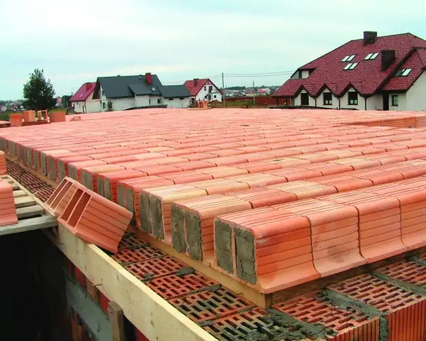 Budowa stropu ackermana z pustaków ceramicznych. W tle domy jednorodzinne.