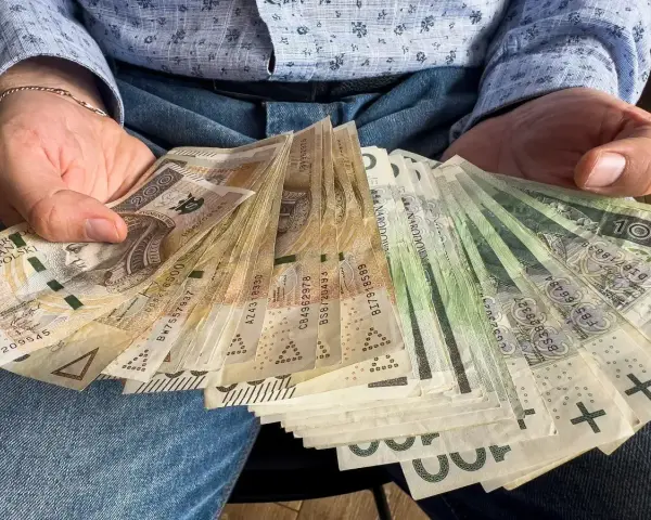 Ręce trzymające plik banknotów 100 zł i 200 zł. To może być darowizna 100 tysięcy od rodziców na nowy dom.