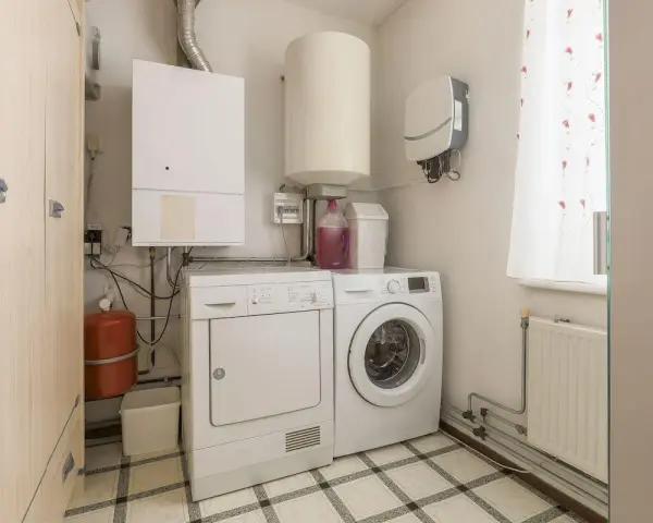 Funkcjonalne pomieszczenie gospodarcze z pralką, suszarką, bojlerem i szafą.