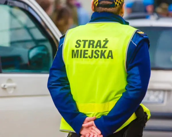 Strażnik miejski w kamizelce odblaskowej stoi obok samochodu.
