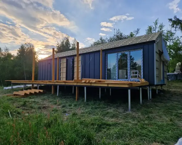 Nowy bungalow na palach, z drewnianym tarasem i dużymi oknami, w trakcie budowy.