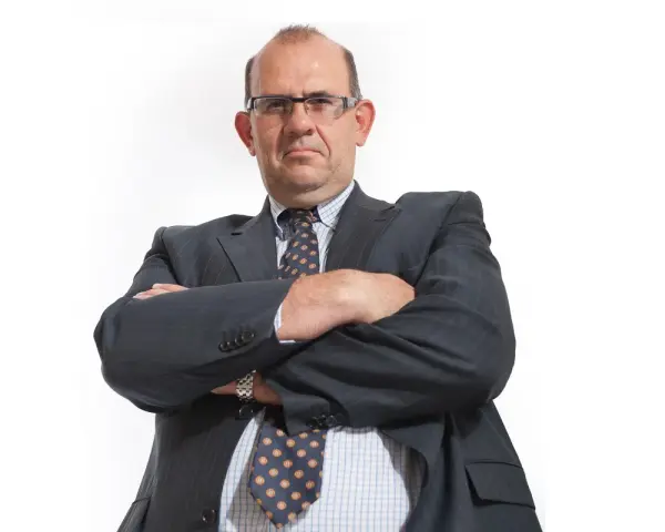 Mężczyzna w garniturze i okularach ze skrzyżowanymi rękami.