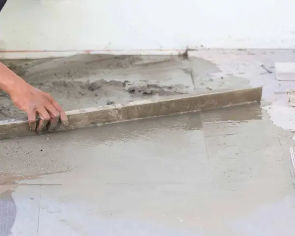 Ręka wyrównuje świeży beton, tworząc idealnie gładką podłogę na gruncie.