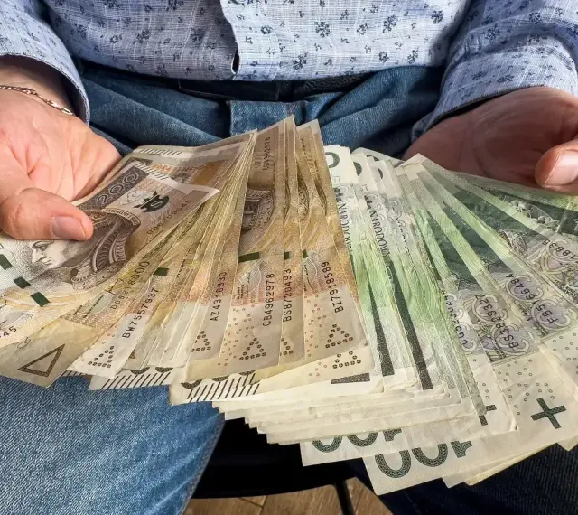 Ręce trzymające plik banknotów 100 zł i 200 zł. To może być darowizna 100 tysięcy od rodziców na nowy dom.