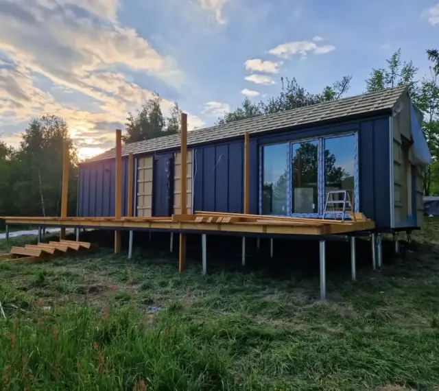 Nowy bungalow na palach, z drewnianym tarasem i dużymi oknami, w trakcie budowy.