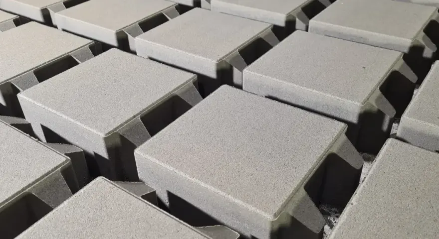 Szare, betonowe kostki brukowe ułożone w rzędach, gotowe do budowy ścieżki. Różne rodzaje kostki brukowej czekają na zastosowanie.