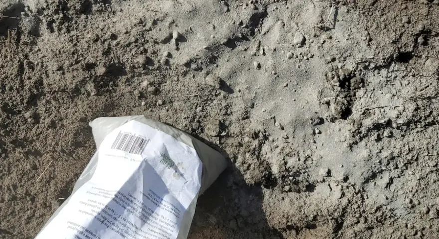 Opakowanie mączki bazaltowej leży na ziemi, gotowe do zastosowania w ogrodzie.