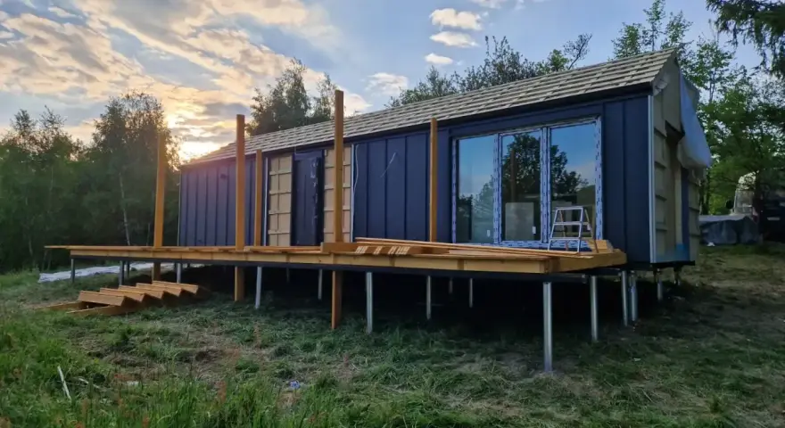 Nowy bungalow na palach, z drewnianym tarasem i dużymi oknami, w trakcie budowy.