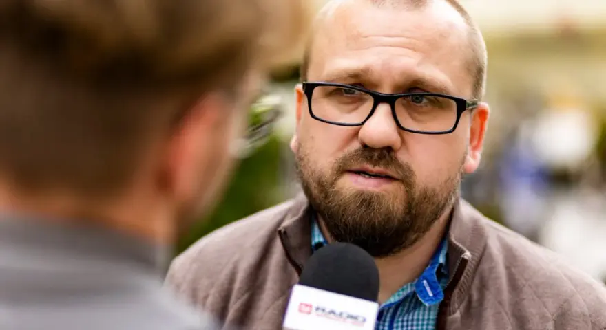 Mężczyzna w okularach udziela wywiadu mikrofonowi radiowemu.