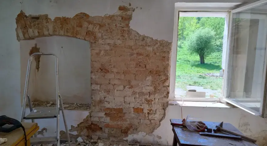 Odkryty mur pruski w trakcie remontu. Widać cegły, gruz, drabinę i narzędzia.