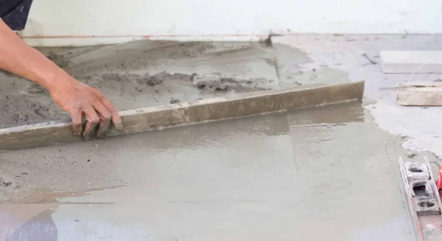 Ręka wyrównuje świeży beton, tworząc idealnie gładką podłogę na gruncie.