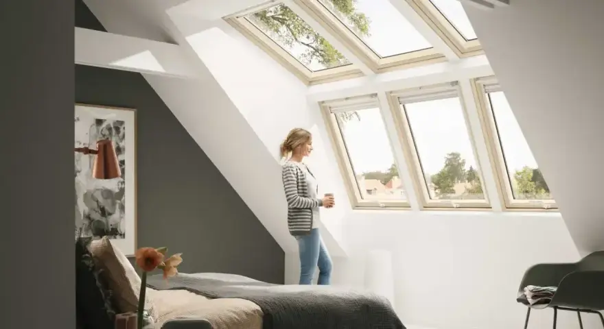 Kobieta w sypialni pod jasną, nowoczesną lukarną dachową, podziwia widok.
