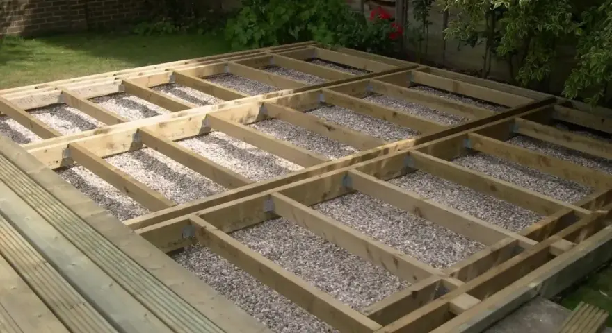Drewniana konstrukcja pod taras z widocznymi legarami i podsypką żwirową. Wymiary legarów są kluczowe dla stabilności.