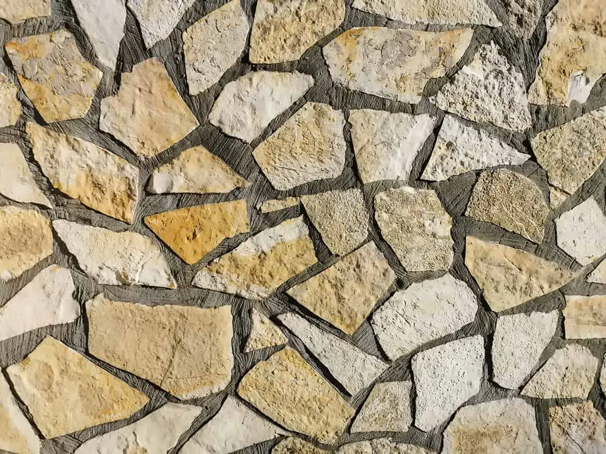 Chropowata ściana z nieregularnych, żółtawych i białych kamieni. Piaskowiec tworzy naturalną mozaikę.
