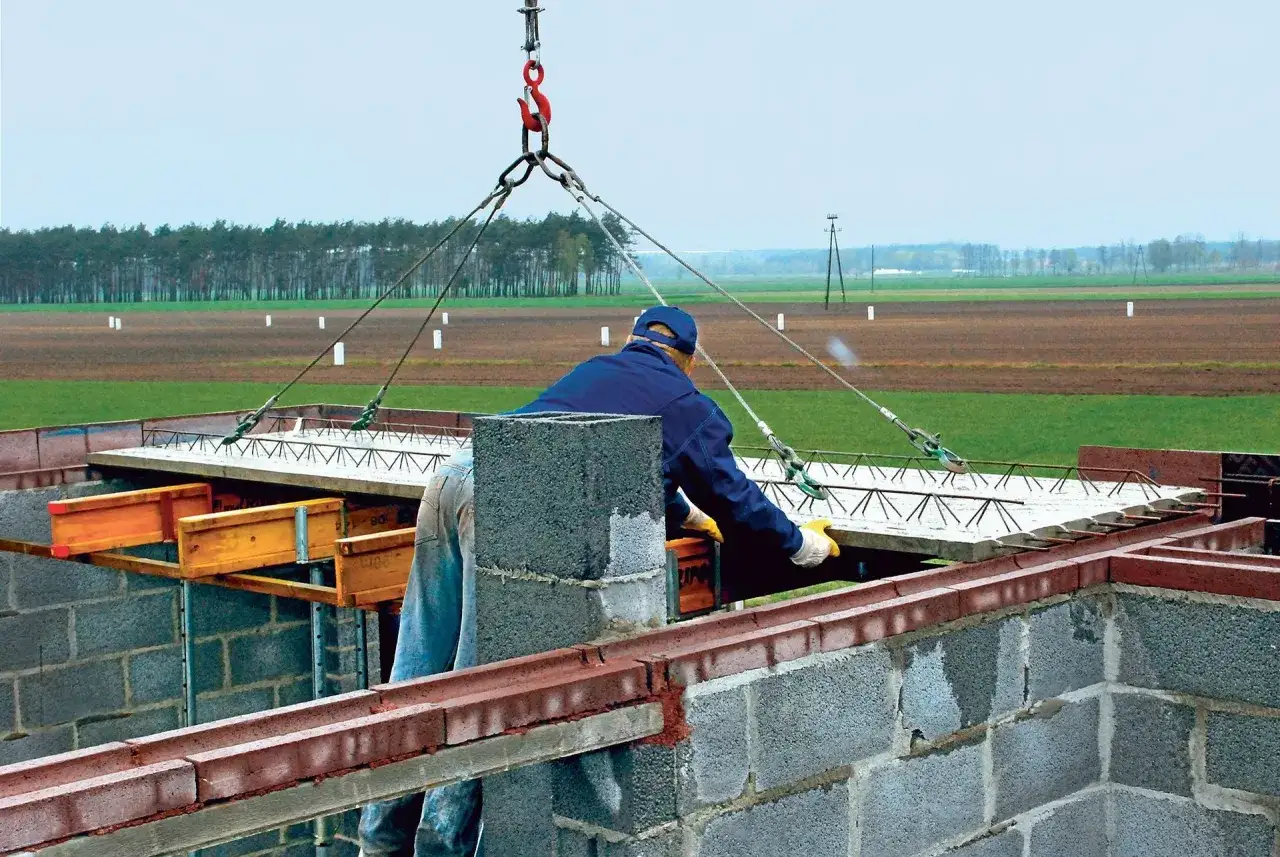 Pracownik kieruje opuszczaniem stropu filigran, który jest podnoszony przez dźwig.