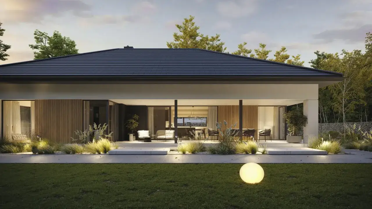 Nowoczesny bungalow z dużymi przeszkleniami i tarasem, otoczony zielenią i oświetlony kulistą lampą.